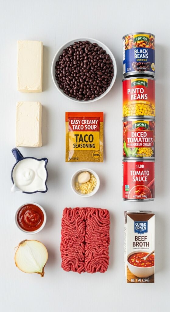 An overhead flat-lay of ingredients for creamy taco soup, including ground beef, canned beans and tomatoes, cream cheese, taco seasoning, and broth.